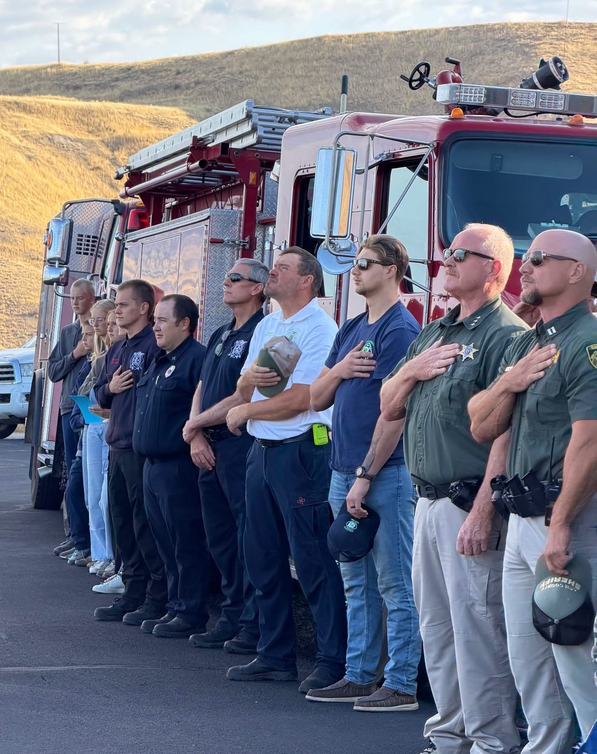 Gem County firefighters and sheriff's deputies standing with hands over hearts in front of a fire engine